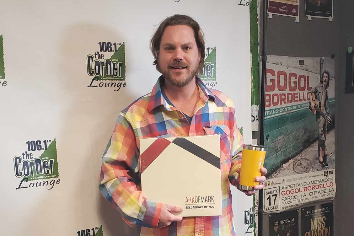 Mark Coffman smiles into camera holding travel mug and new album.