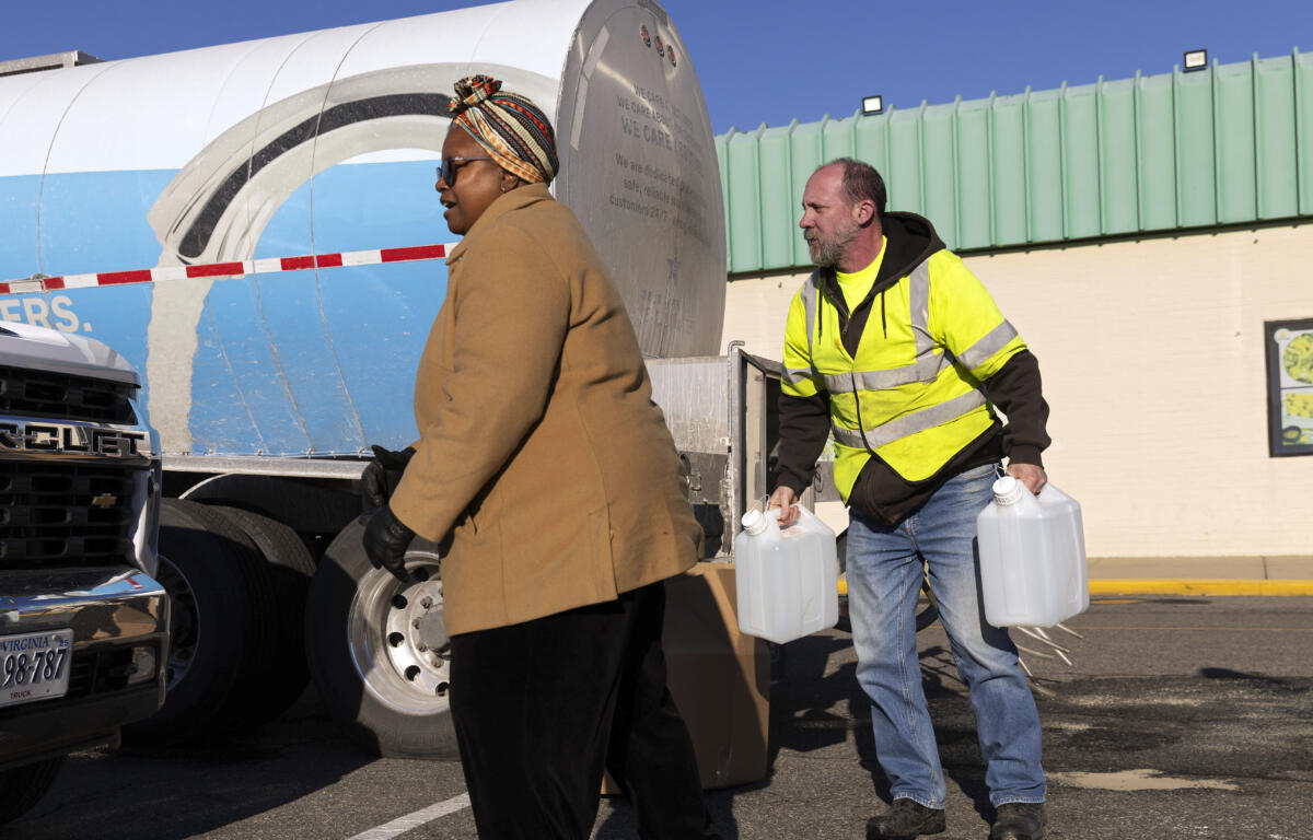 Adam Guay carries jugs of water for Theresa Slayton from a tank truck at Southside Plaza in Richmond during water outage crisis. (AP Photo/Ryan Kelly)