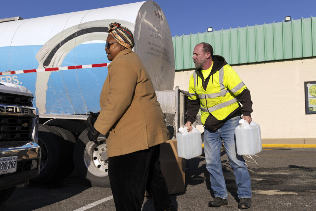Adam Guay carries jugs of water for Theresa Slayton from a tank truck at Southside Plaza in Richmond during water outage crisis. (AP Photo/Ryan Kelly)