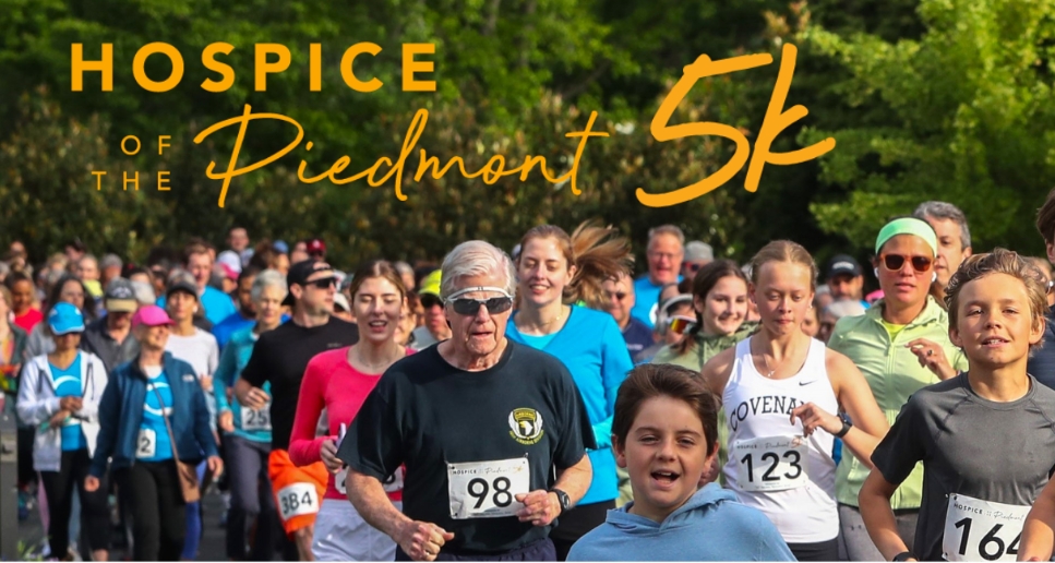 Runners crowded at a 5k charity race, with an orange 'Hospice of the Piedmont 5k' banner across the top of the image.