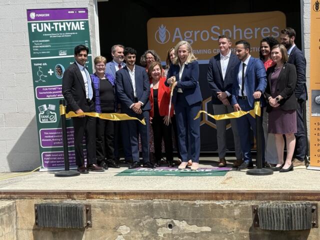 Group of people cutting a yellow ribbon at AgroSpheres launch, with banners on the sides.