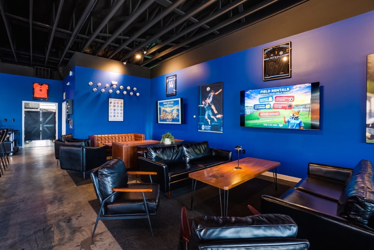 Cozy sports lounge with blue walls, black leather seating, and wooden tables, plus wall TVs and posters.