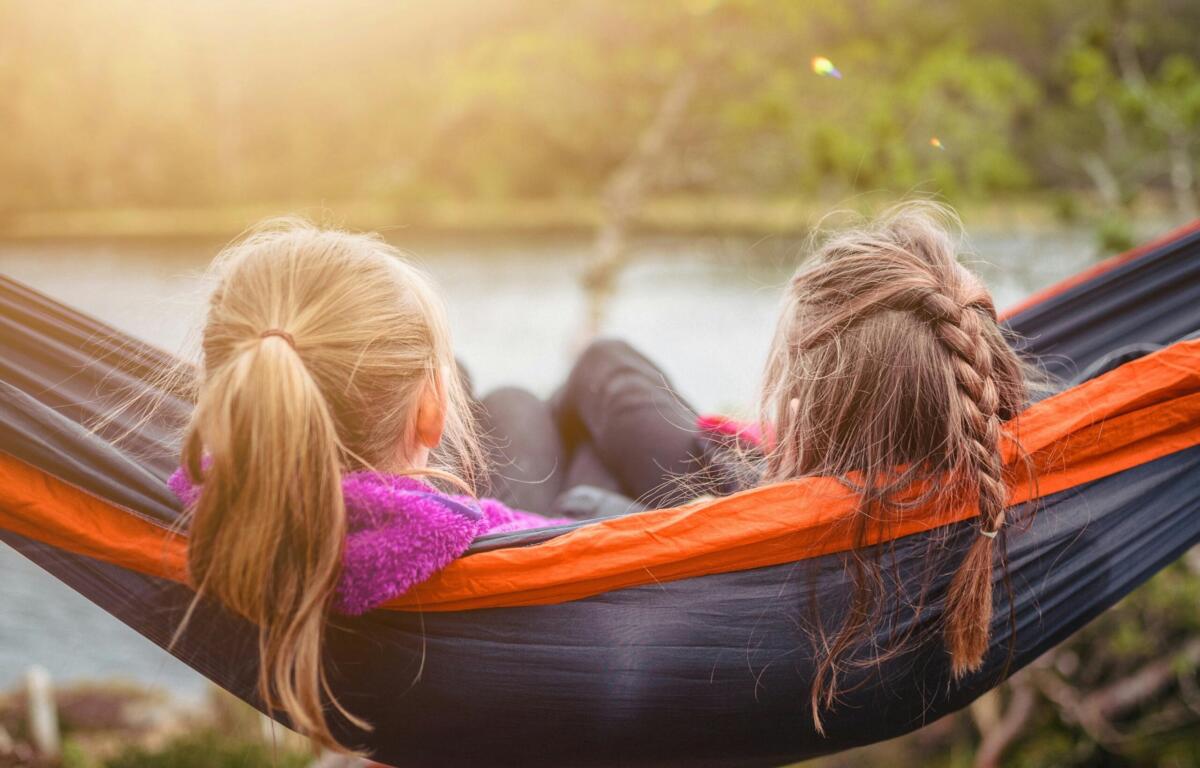 Two people lie in a red-and-black hammock outdoors at sunset, facing away from the camera.