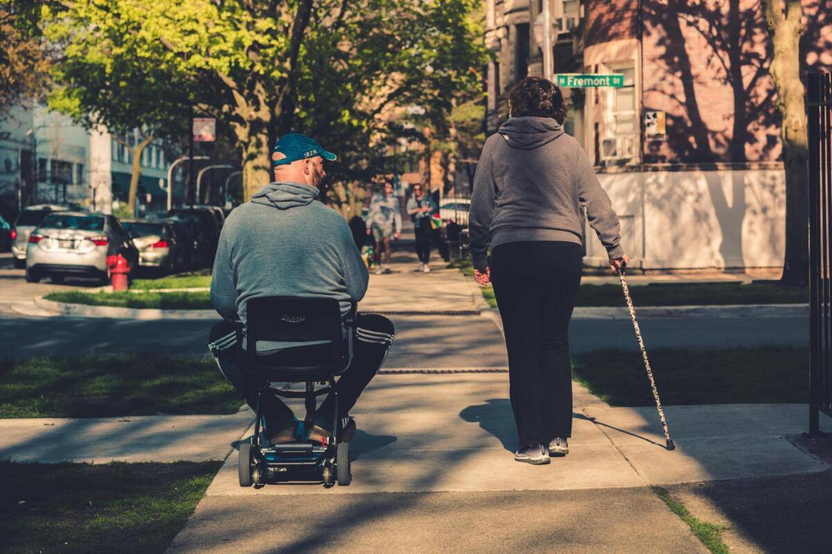 Man in wheelchair walking with woman with guiding cane