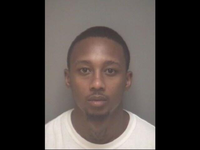 Mugshot of a young man with short hair and a light goatee, wearing a white shirt, facing the camera against a gray backdrop.