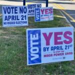 Campaign signs on a grassy roadside urging votes for April 21, some say 'Vote No' and others 'Yes' in bold letters.