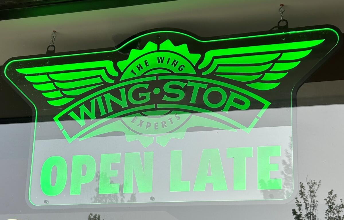 Neon green Wingstop sign with wing logo and OPEN LATE text in window.