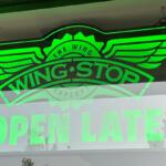 Neon green Wingstop sign with wing logo and OPEN LATE text in window.