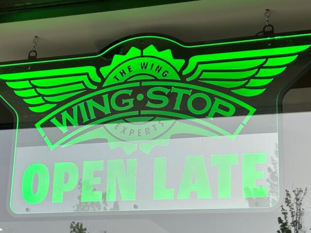 Neon green Wingstop sign with wing logo and OPEN LATE text in window.