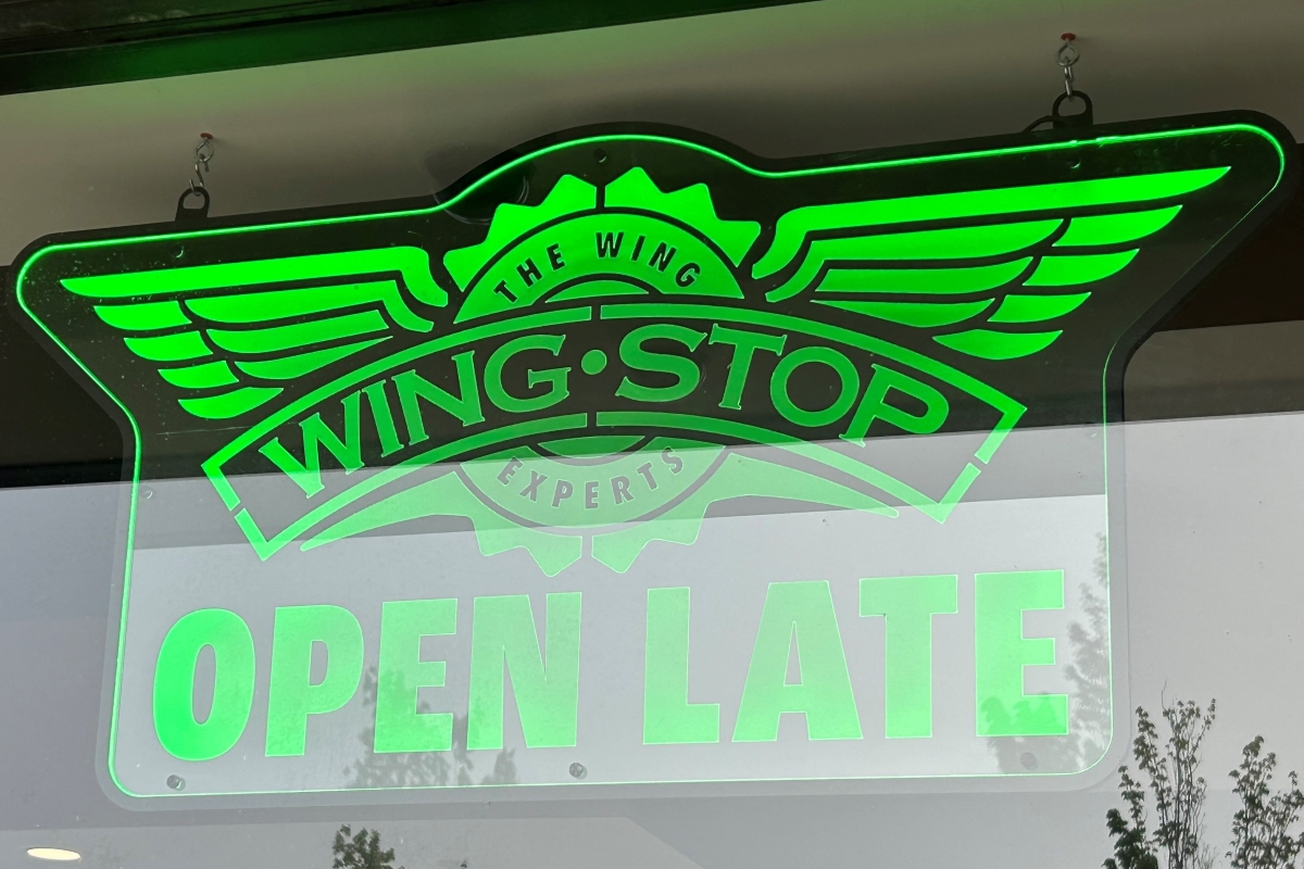 Neon green Wingstop sign with wing logo and OPEN LATE text in window.