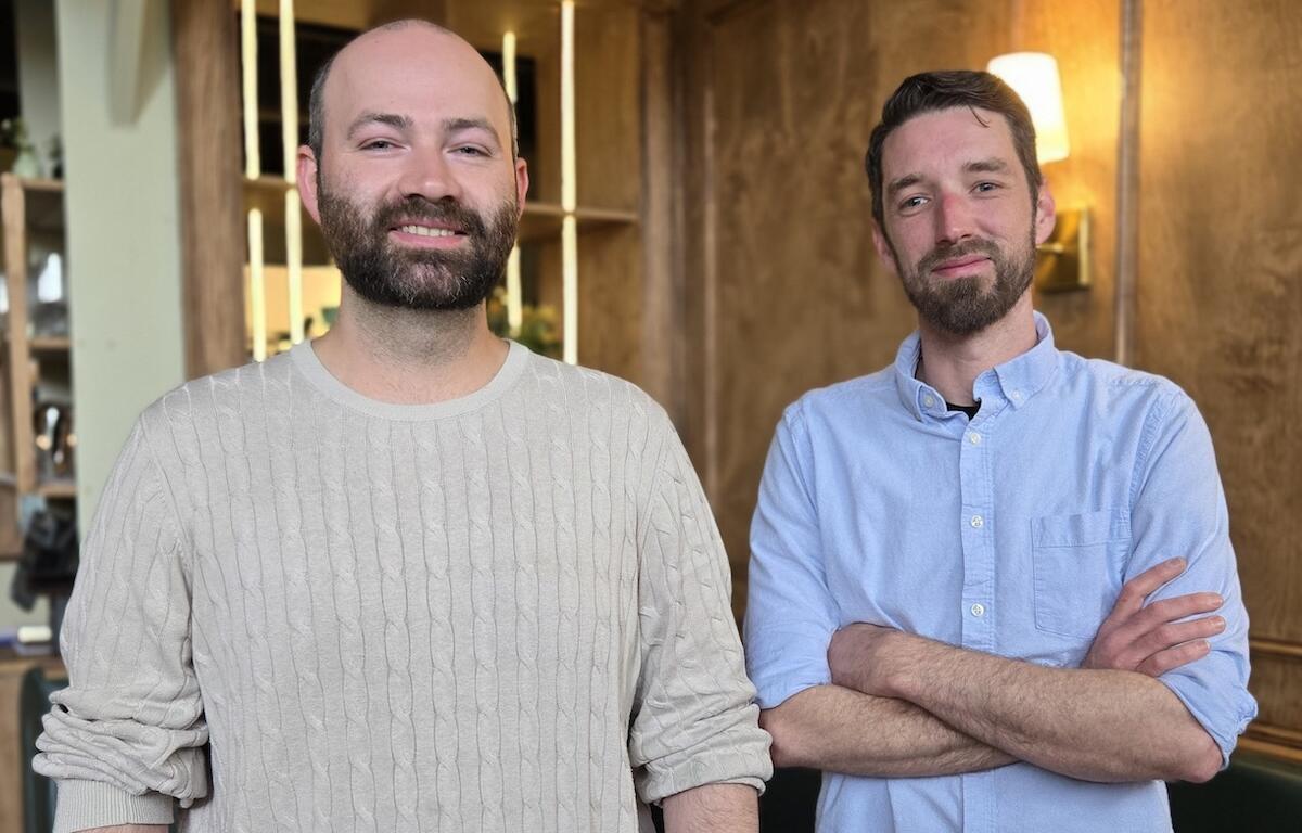 Two bearded men stand in a modern office, smiling at the camera.