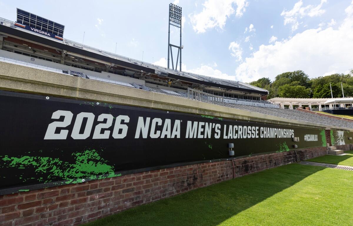 Stadium view with a large banner reading '2026 NCAA Men's Lacrosse Championships' along a brick wall and green field nearby, under a bright sky