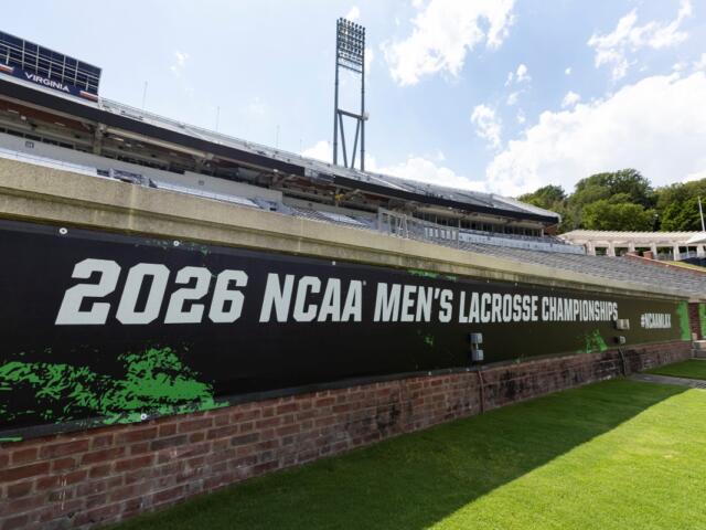 Stadium view with a large banner reading '2026 NCAA Men's Lacrosse Championships' along a brick wall and green field nearby, under a bright sky
