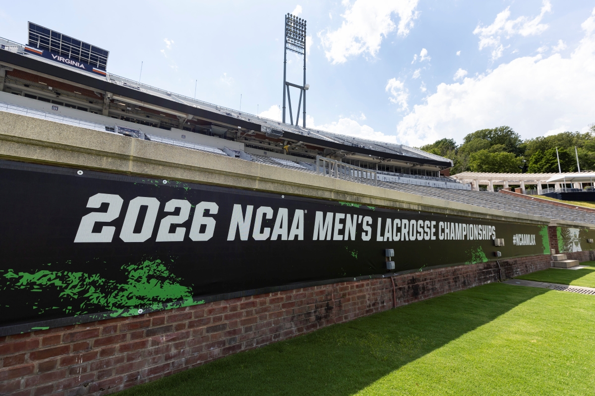 Stadium view with a large banner reading '2026 NCAA Men's Lacrosse Championships' along a brick wall and green field nearby, under a bright sky