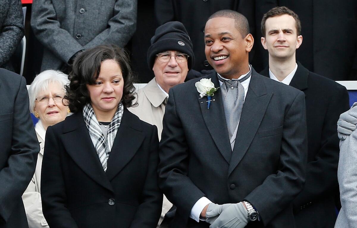 Smiling man in a dark suit with a white boutonniere, flanked by others in winter coats in a formal group photo.