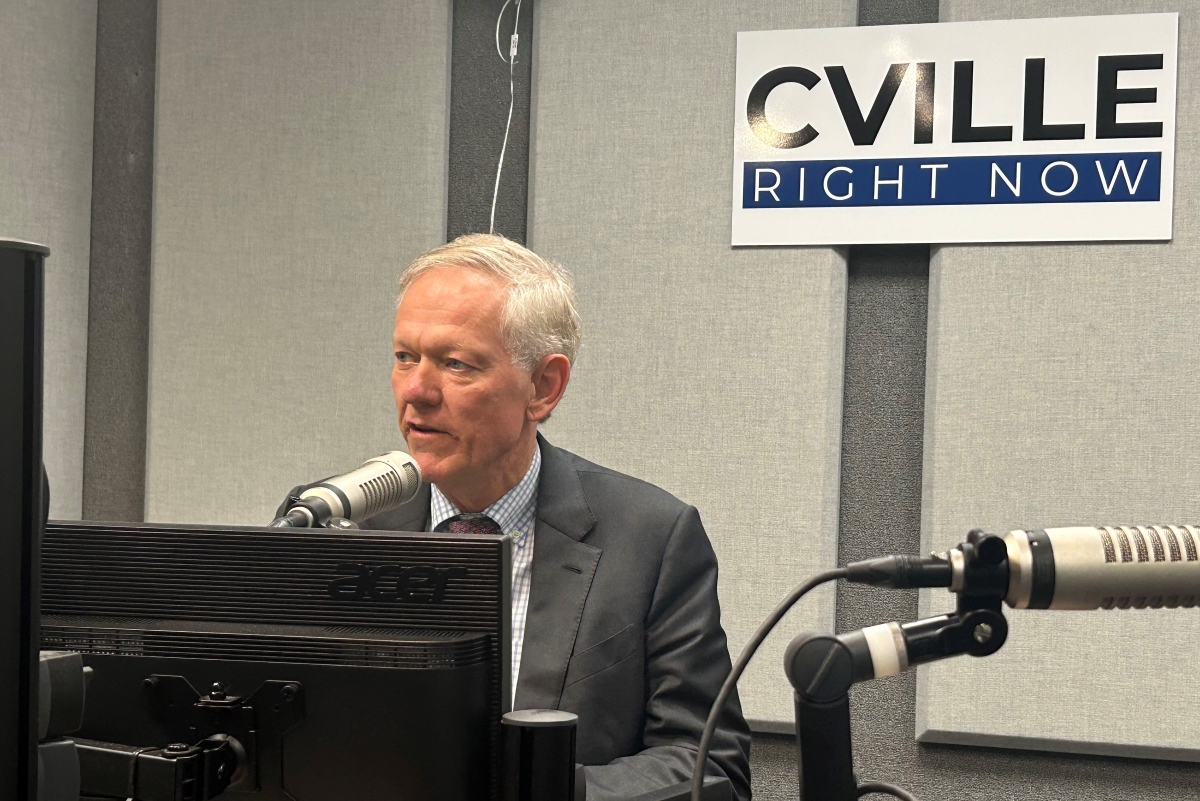 Man in a suit speaks into a studio microphone at a radio station, with a 'CVILLE RIGHT NOW' sign on the wall behind him.
