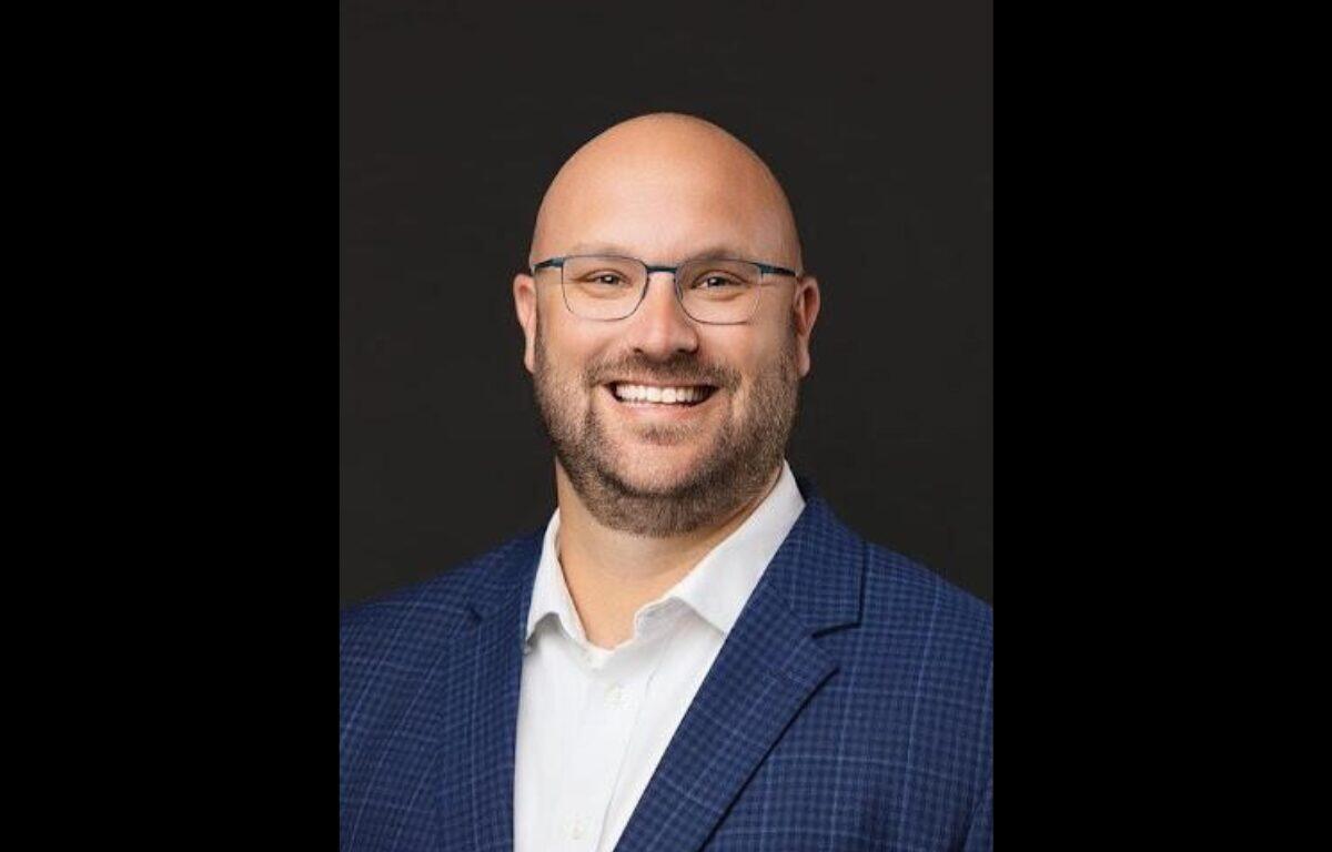 Smiling man in a blue blazer and white shirt against a dark background (professional headshot)