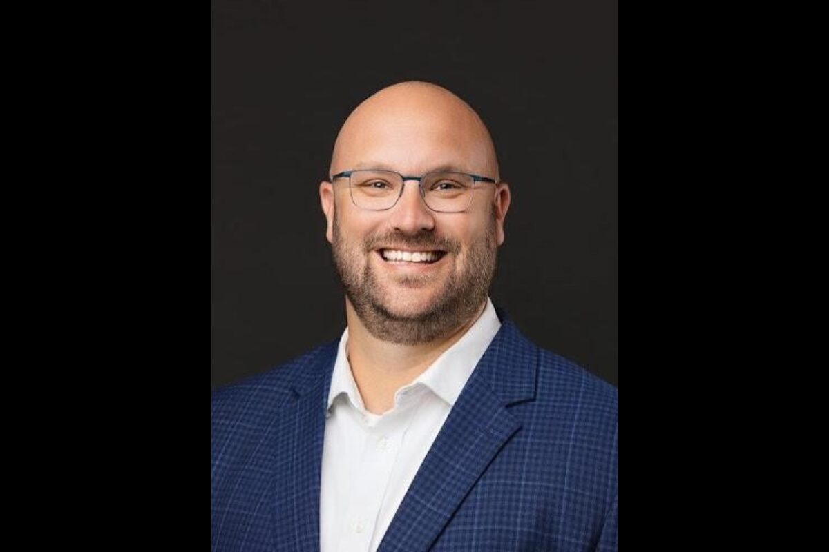 Smiling man in a blue blazer and white shirt against a dark background (professional headshot)