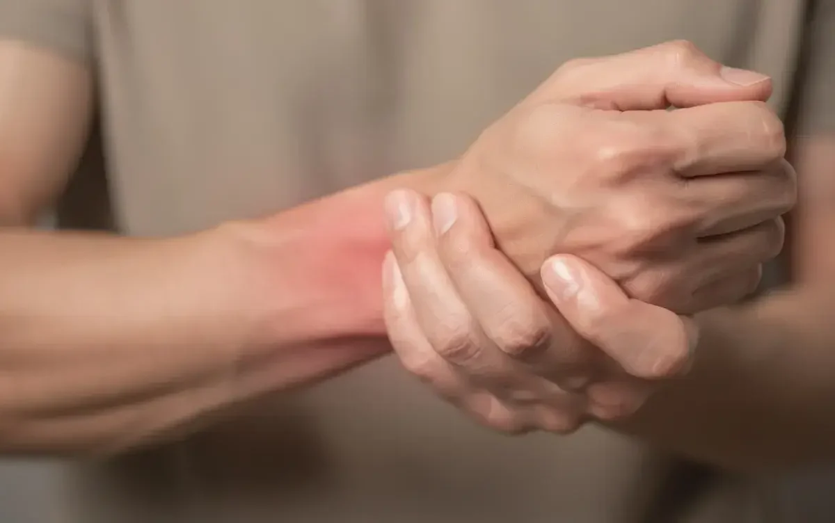 Person's hands clasped around a reddened wrist, indicating wrist pain or strain.