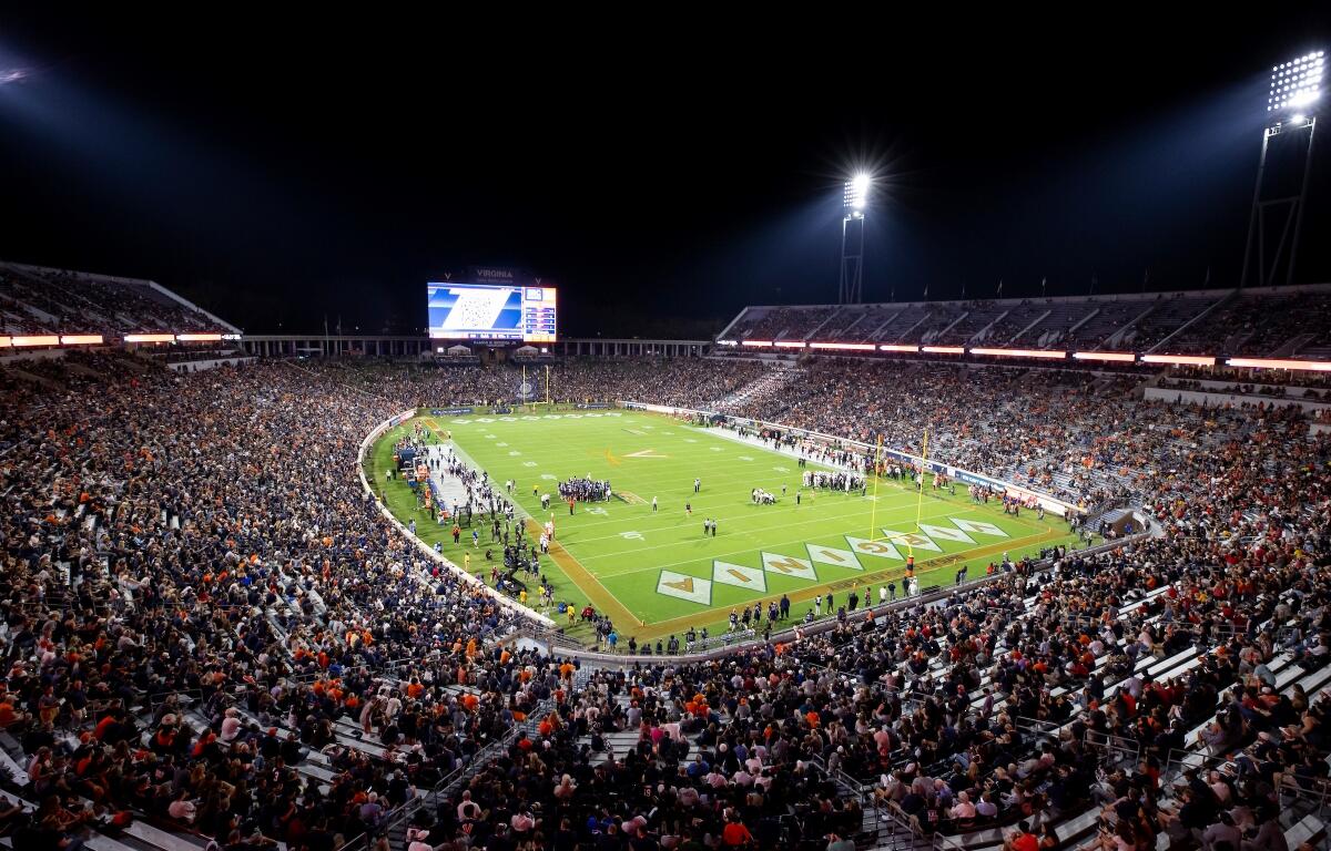 Nighttime football game in a packed outdoor stadium, field lit by tall floodlights with a large crowd in the stands.