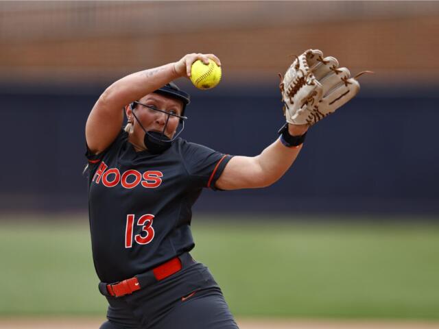 Softball pitcher in black uniform labeled HOOS, number 13, throws a yellow ball with glove raised mid-throw on a field.