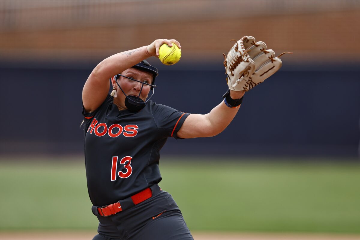 Softball pitcher in black uniform labeled HOOS, number 13, throws a yellow ball with glove raised mid-throw on a field.