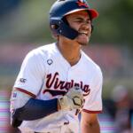 Virginia Cavaliers baseball player in a white jersey and helmet, grimacing as he runs.