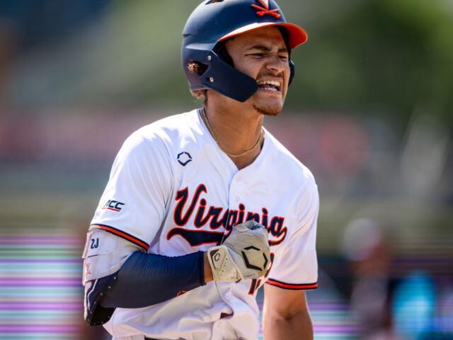 Virginia Cavaliers baseball player in a white jersey and helmet, grimacing as he runs.