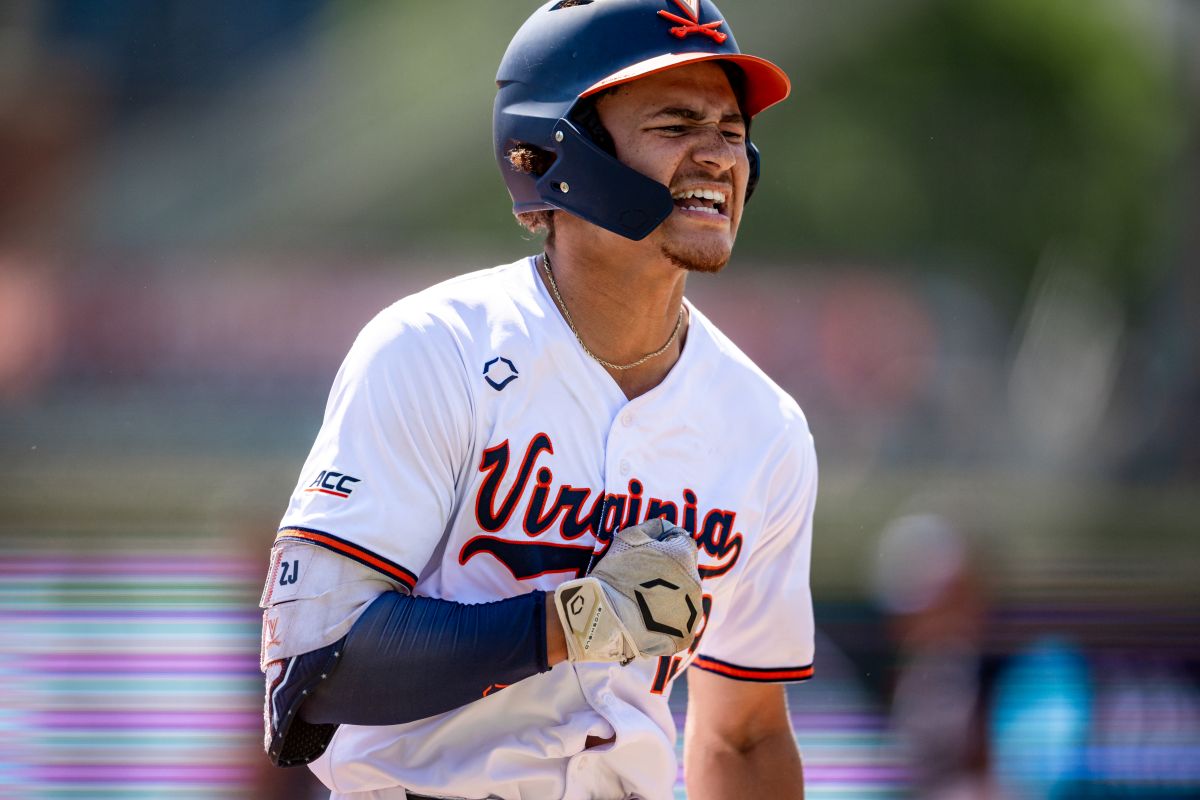 Virginia Cavaliers baseball player in a white jersey and helmet, grimacing as he runs.