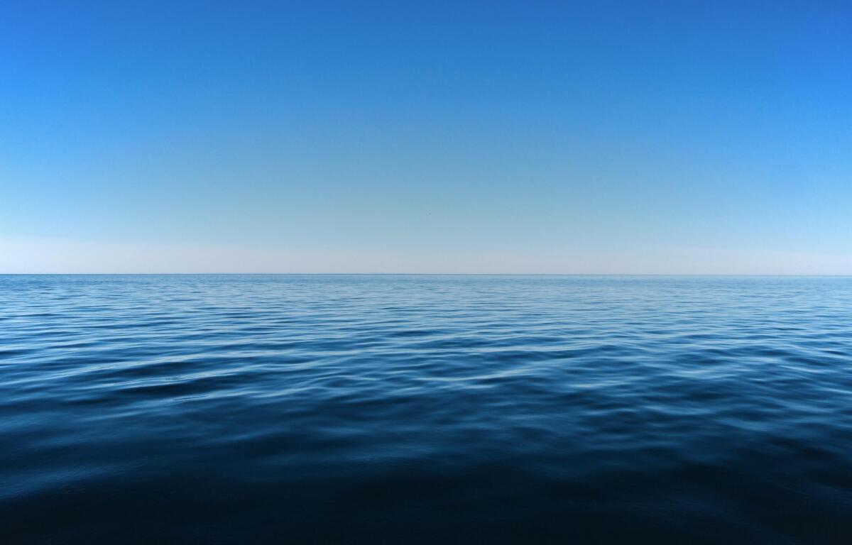 Calm sea at the horizon beneath a clear gradient blue sky, tranquil and expansive.