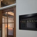 Wooden door with a glass panel next to a white wall; a poster on the wall reads 'THE ENEMY' in large letters.