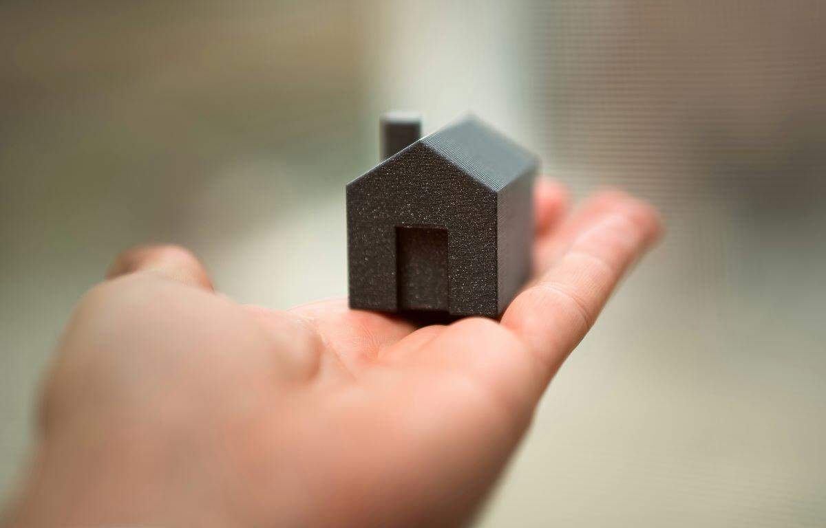 Tiny black house model resting in an open palm, roof and doorway visible