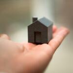 Tiny black house model resting in an open palm, roof and doorway visible