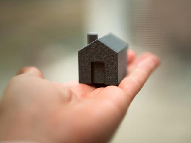 Tiny black house model resting in an open palm, roof and doorway visible
