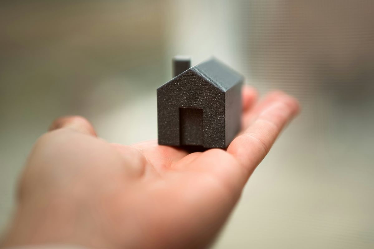 Tiny black house model resting in an open palm, roof and doorway visible