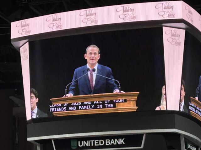 Male speaker at a wooden podium delivering a speech on a large curved LED stage with United Bank signage visible beneath.