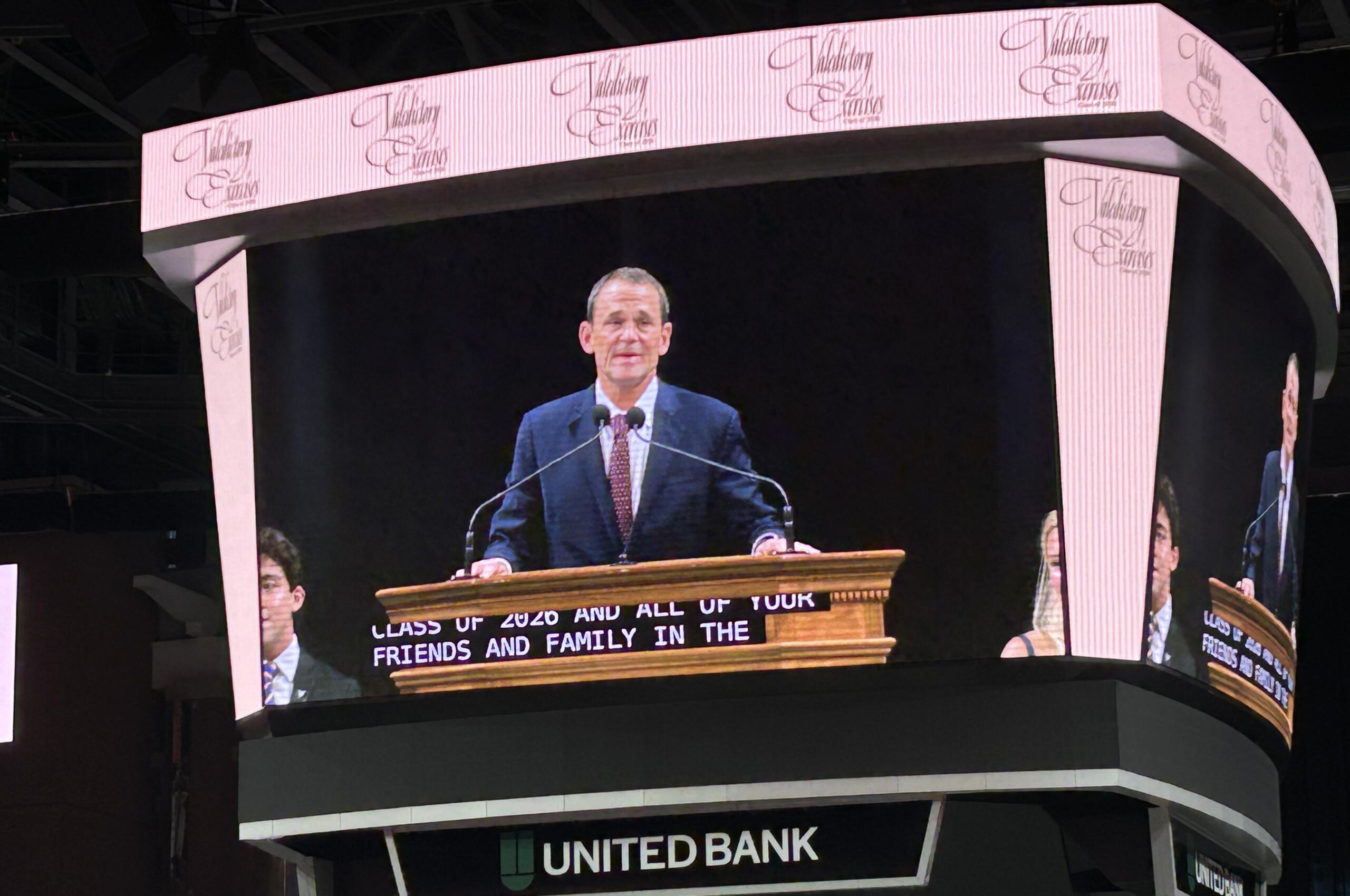 Male speaker at a wooden podium delivering a speech on a large curved LED stage with United Bank signage visible beneath.
