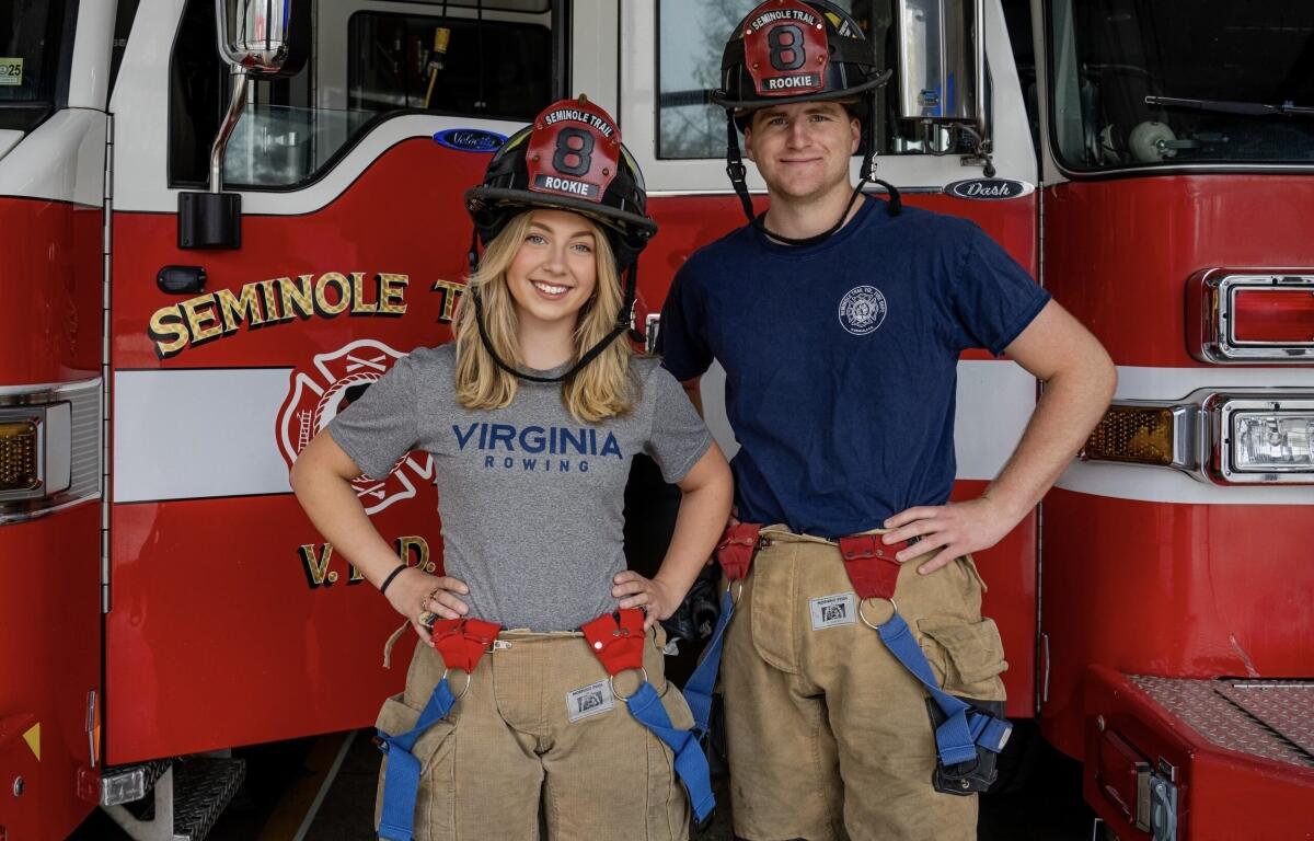 Two firefighters pose in front of a red fire truck, wearing turnout gear and helmets marked Rookie 8.