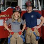 Two firefighters pose in front of a red fire truck, wearing turnout gear and helmets marked Rookie 8.