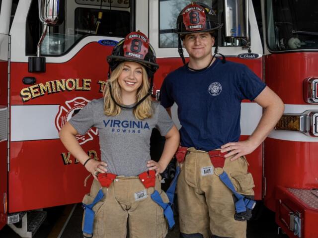 Two firefighters pose in front of a red fire truck, wearing turnout gear and helmets marked Rookie 8.