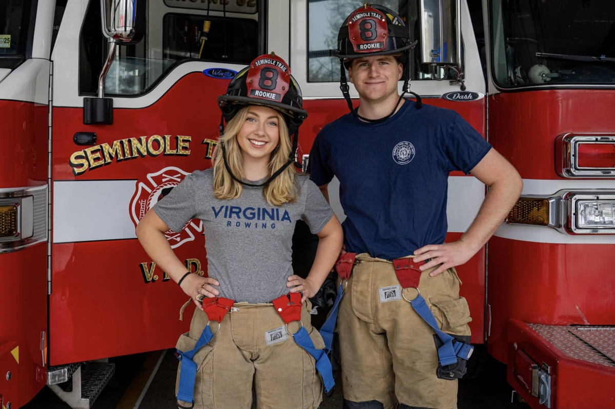 Two firefighters pose in front of a red fire truck, wearing turnout gear and helmets marked Rookie 8.
