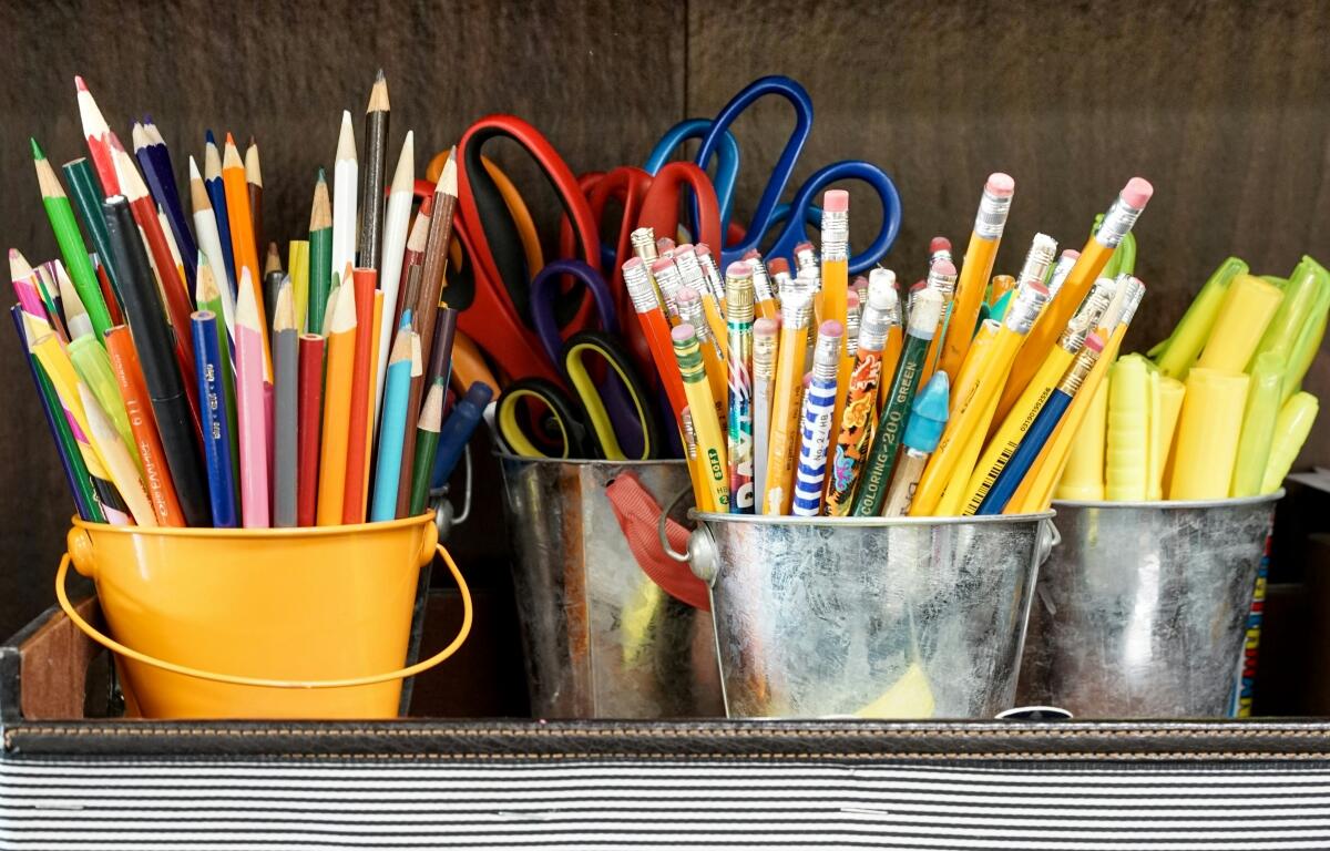 Colorful pencils, scissors, and markers in yellow and metal buckets on a desk, ready for art class.