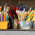 Colorful pencils, scissors, and markers in yellow and metal buckets on a desk, ready for art class.