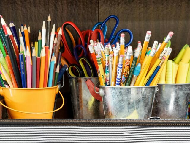 Colorful pencils, scissors, and markers in yellow and metal buckets on a desk, ready for art class.