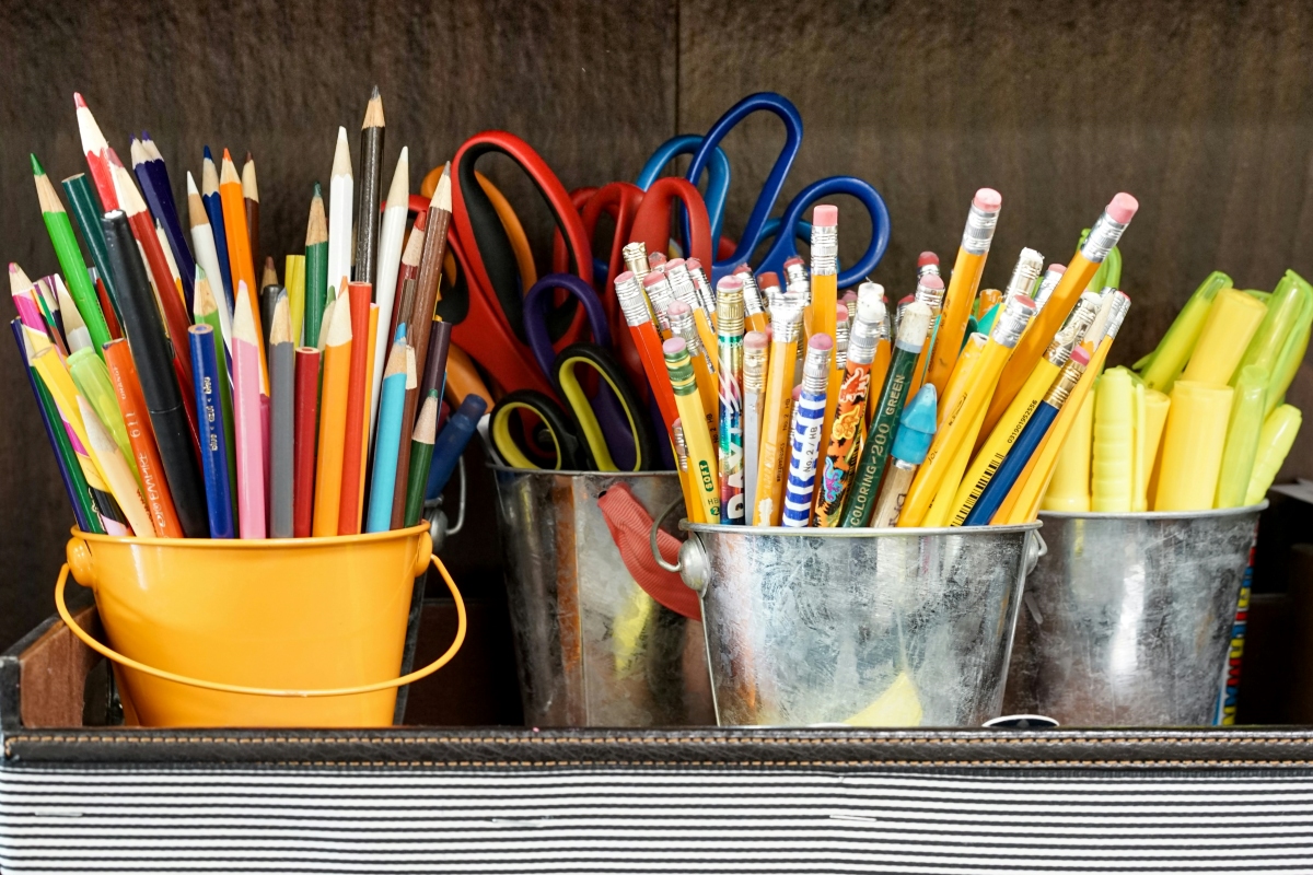 Colorful pencils, scissors, and markers in yellow and metal buckets on a desk, ready for art class.