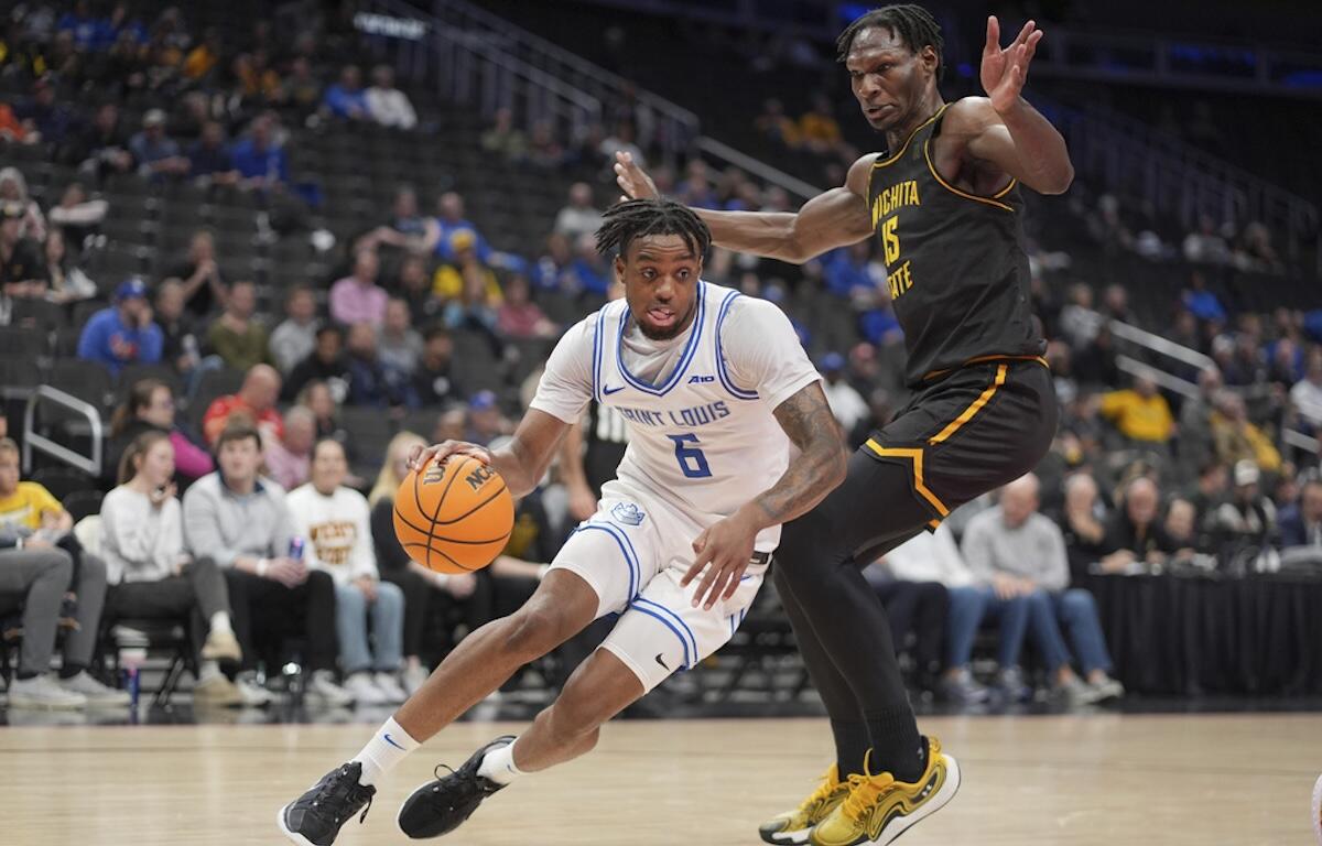Saint Louis player #6 in white dribbles the ball while a Wichita State defender in black and gold reaches in.