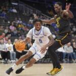 Saint Louis player #6 in white dribbles the ball while a Wichita State defender in black and gold reaches in.