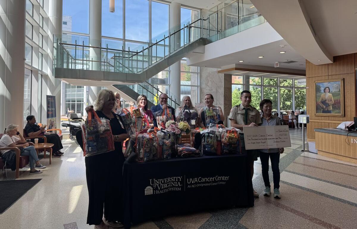 Group of people stand behind a table full of gift baskets in a bright hospital lobby, with a UVA Cancer Center sign on the table.
