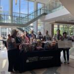 Group of people stand behind a table full of gift baskets in a bright hospital lobby, with a UVA Cancer Center sign on the table.