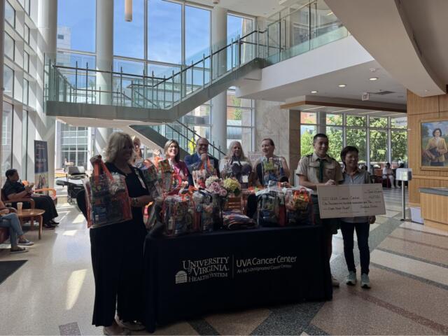 Group of people stand behind a table full of gift baskets in a bright hospital lobby, with a UVA Cancer Center sign on the table.